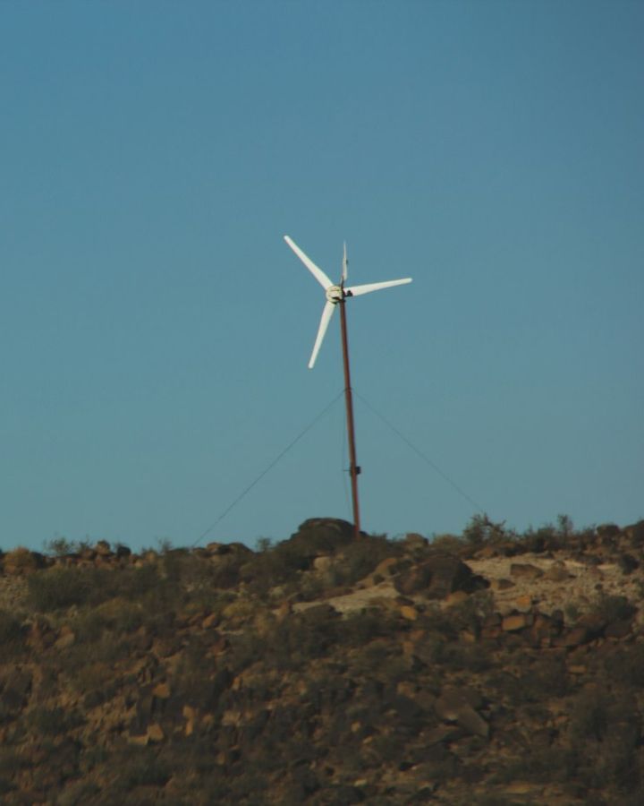 A small white wind turbine on a hill under a clear sky